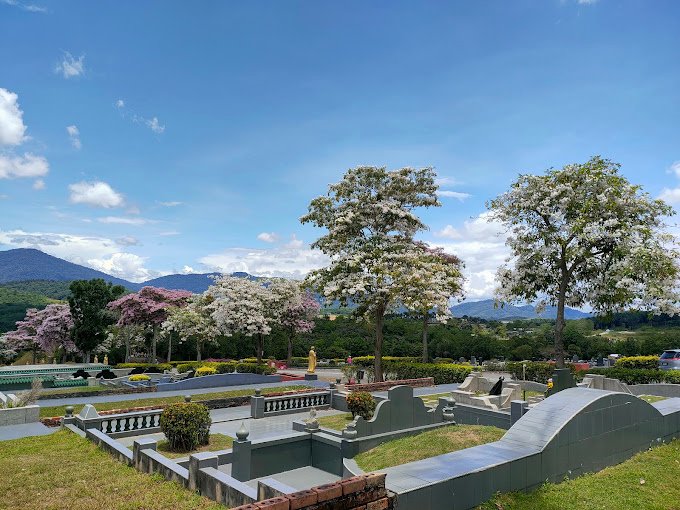 Landscaped memorial grounds framed by flowering trees and hills at Nirvana Semenyih