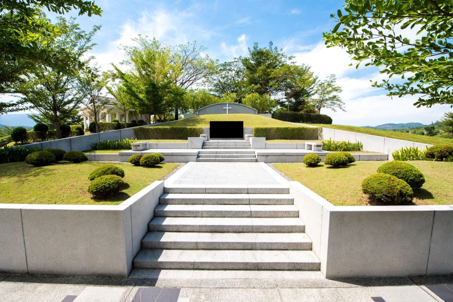 Christian burial plot with a white cross, hedges and mountain backdrop