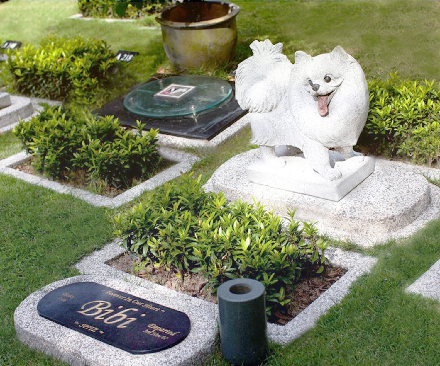 Pet burial plot with a sculpted dog memorial and landscaped planting